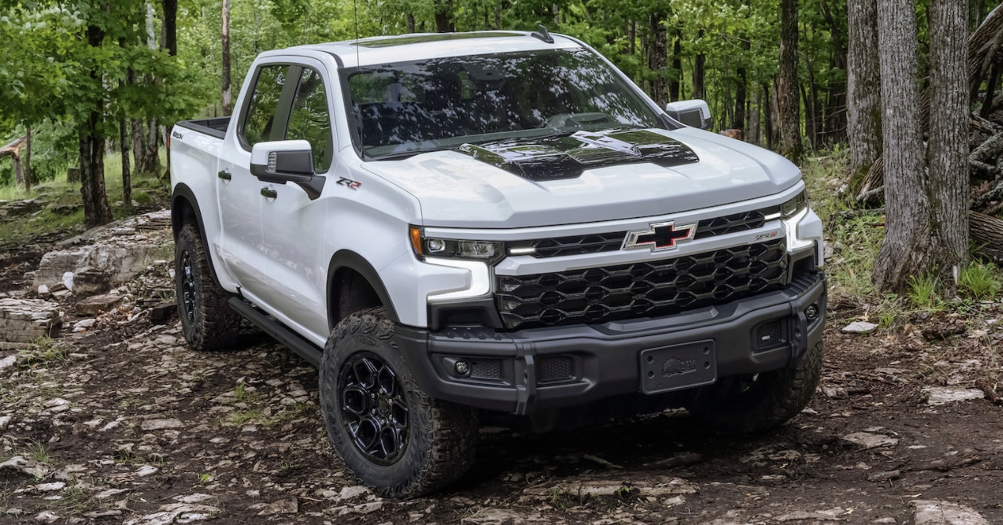 2023 Chevrolet Silverado in the country parked on a hill with multch and trees in the background.