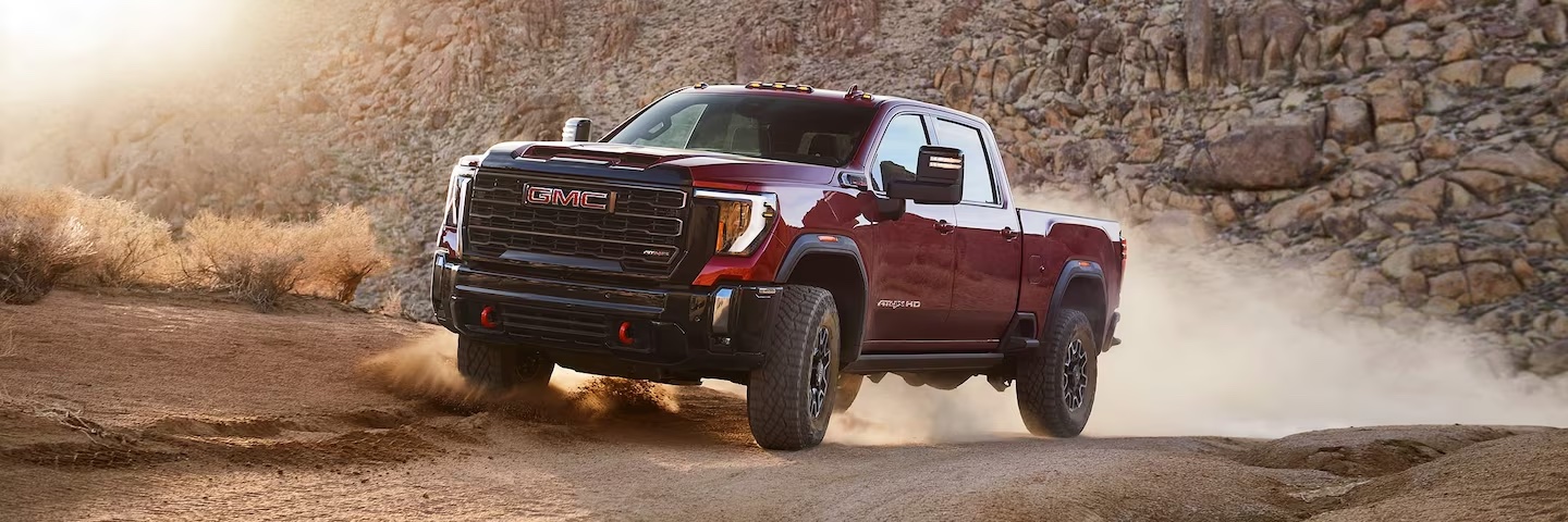 The 2024 GMC 2500HD AT4X in red driving on a dirt road.